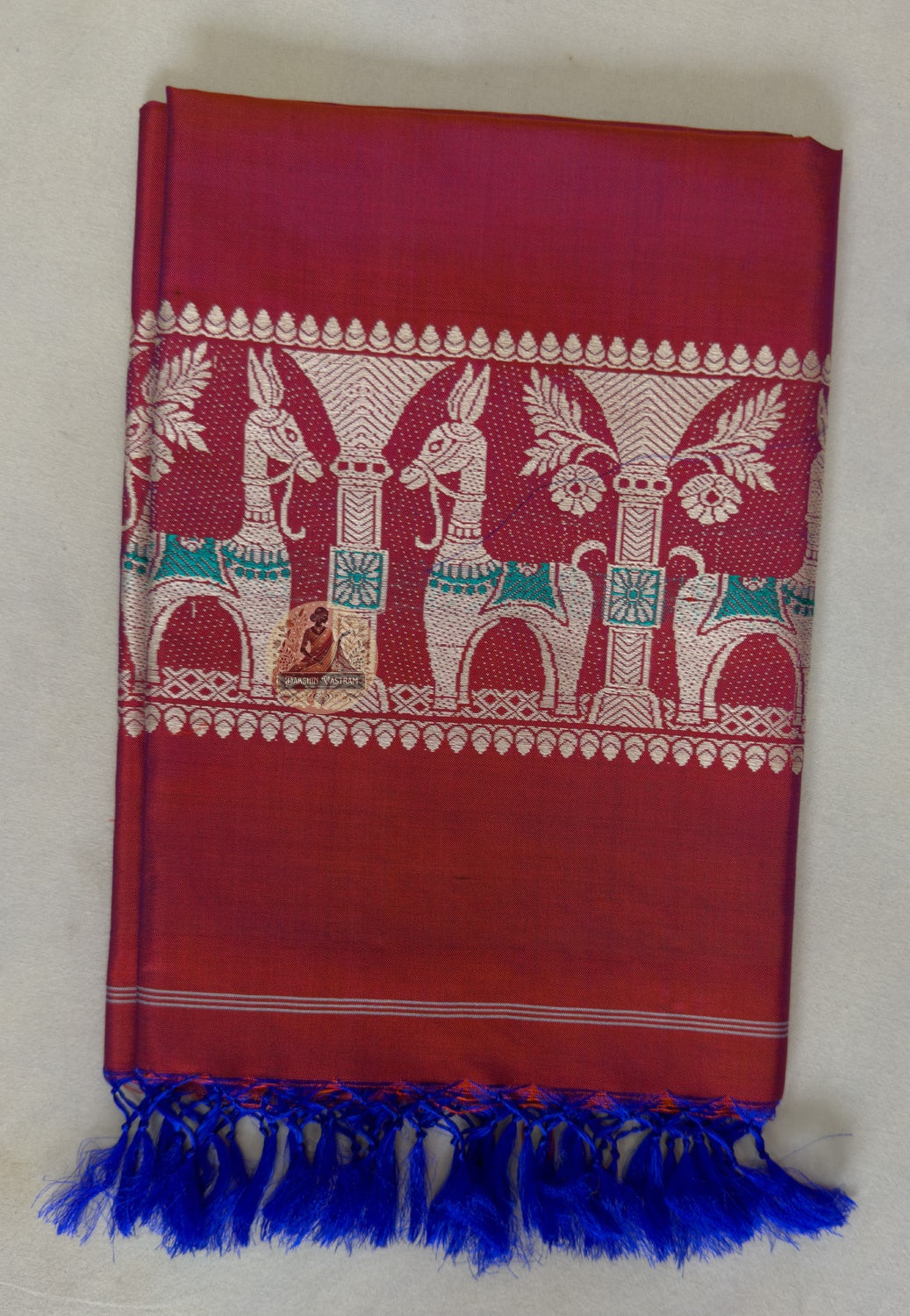 Full flat lay of handwoven Baluchari silk stole in crimson red – complete view of buti body, multicolour court narrative border and royal blue silk tassel fringe, Bishnupur weave
