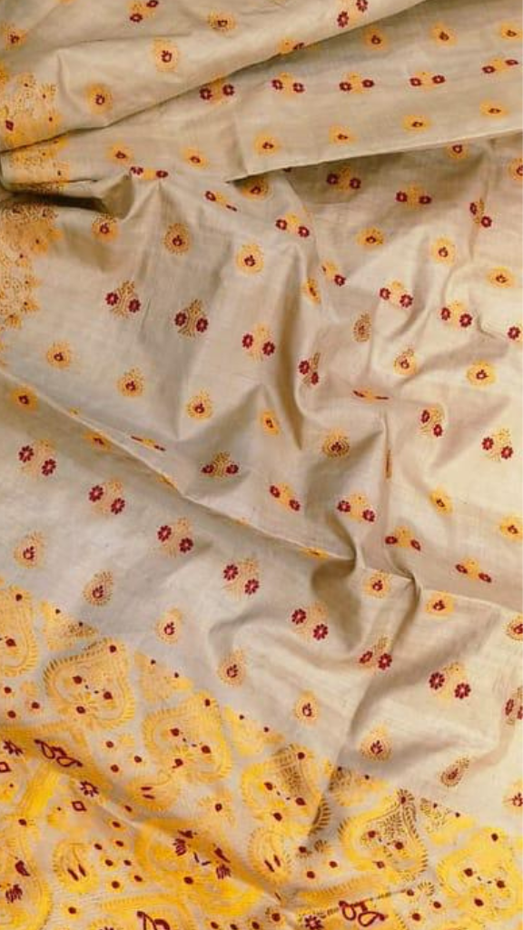 A close-up of a draped fabric, likely a saree, featuring a light beige base with small orange and red floral prints, and a prominent yellow border with detailed orange and red embroidery.